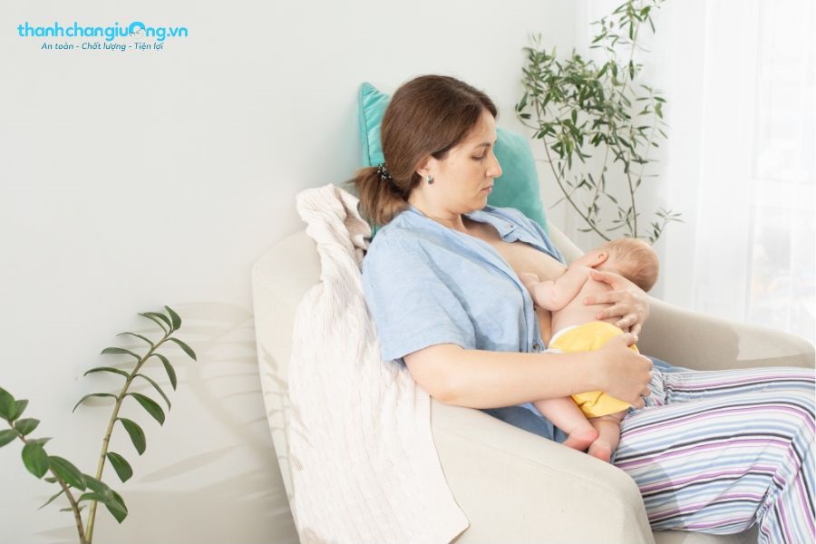 Mẹ ngồi tựa lưng thoải mái, ổn định rồi nhẹ nhàng nâng bé lên và cho bé bú